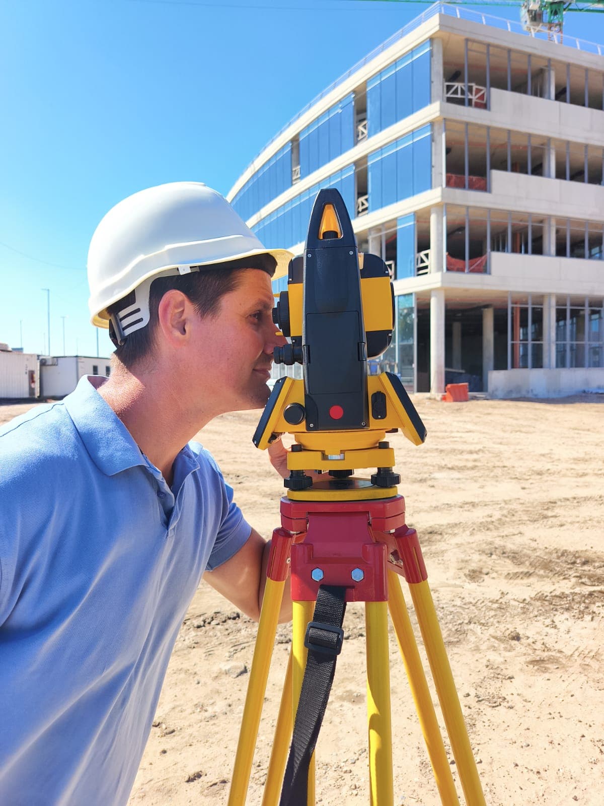 Pablo Venerus, agrimensor, con casco realizando un relevamiento con estación total frente a un edificio en construcción